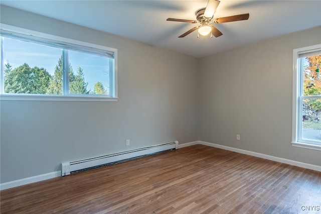 empty room featuring a wealth of natural light, ceiling fan, wood-type flooring, and baseboard heating