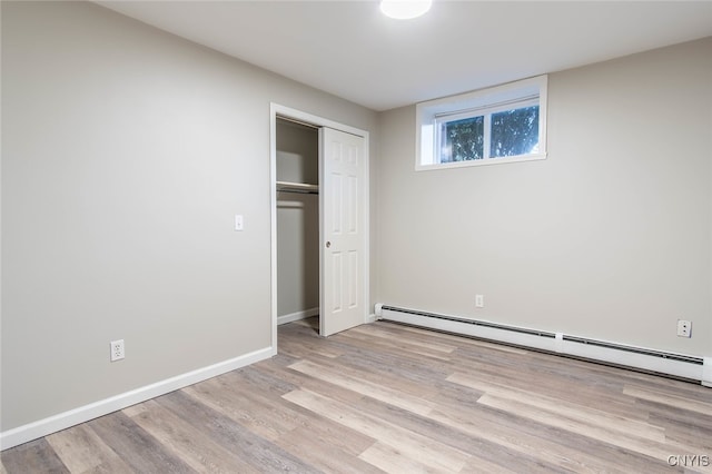 unfurnished bedroom featuring a closet, baseboard heating, and light wood-type flooring