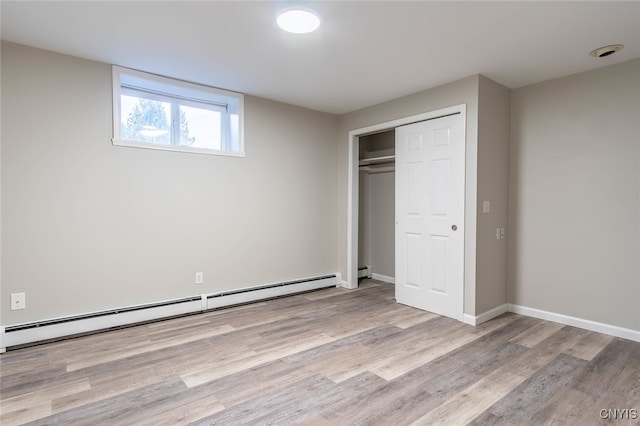 unfurnished bedroom with a baseboard heating unit, light hardwood / wood-style flooring, and a closet