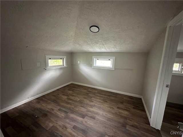 spare room featuring a textured ceiling, vaulted ceiling, and dark hardwood / wood-style floors