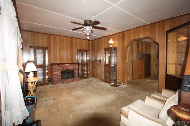 carpeted living room with ceiling fan, wooden walls, and a fireplace