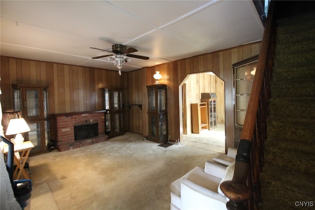 carpeted living room featuring wooden walls, a fireplace, and ceiling fan