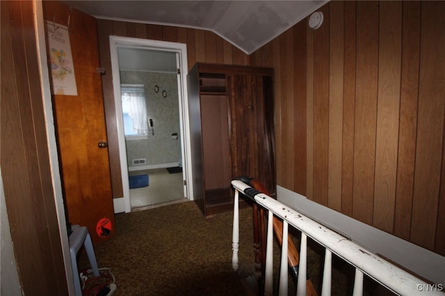 corridor with lofted ceiling, wooden walls, and carpet flooring