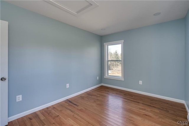 spare room with baseboards, attic access, and wood finished floors