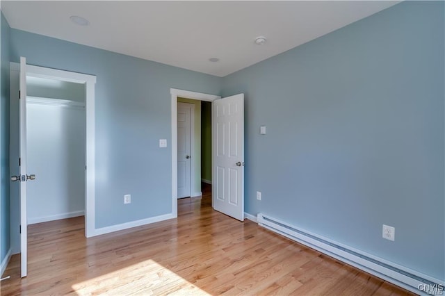 unfurnished bedroom featuring a closet, light wood finished floors, baseboards, and baseboard heating
