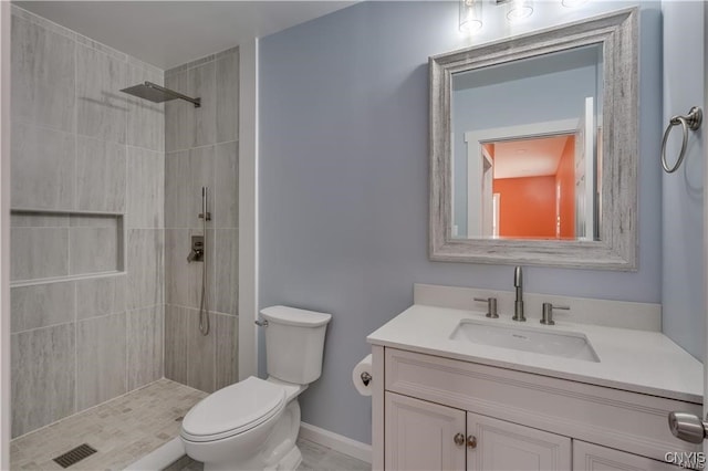 bathroom with a tile shower, vanity, and toilet