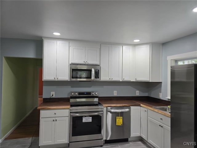 kitchen with white cabinetry, wooden counters, stainless steel appliances, and wood-type flooring