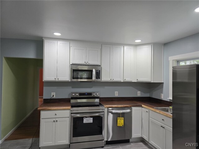 kitchen with recessed lighting, stainless steel appliances, wooden counters, and white cabinets
