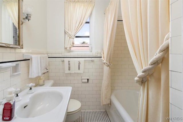 bathroom featuring shower / bath combination with curtain, toilet, tile walls, a wainscoted wall, and a sink
