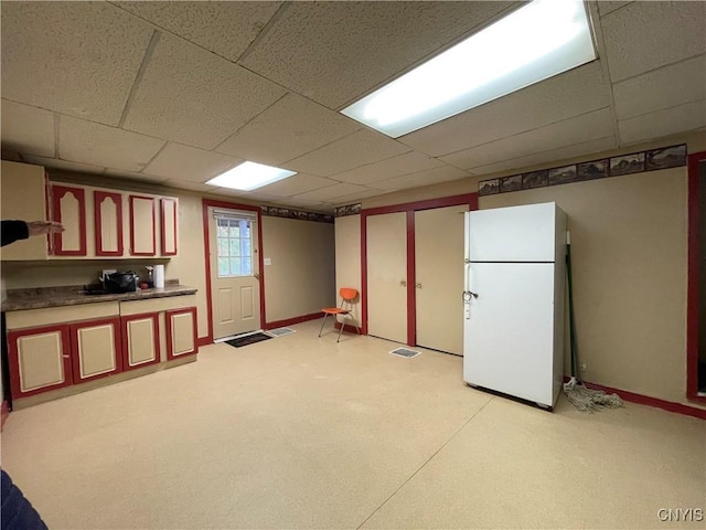 basement featuring a drop ceiling and white fridge