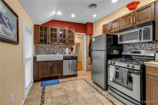 kitchen featuring sink, light tile patterned flooring, backsplash, stainless steel appliances, and lofted ceiling