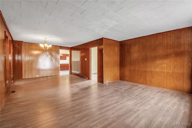 empty room featuring a chandelier, light hardwood / wood-style flooring, and wood walls