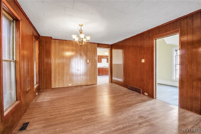 spare room featuring wooden walls, light hardwood / wood-style flooring, and a notable chandelier