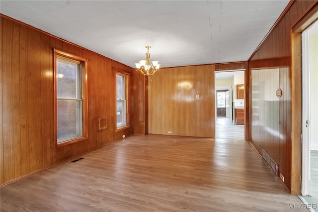 spare room with wood walls, an inviting chandelier, and light wood-type flooring