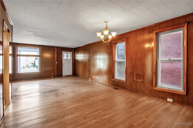 spare room featuring wooden walls, light hardwood / wood-style flooring, and a chandelier