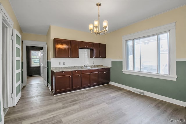 kitchen with light stone counters, a notable chandelier, light wood-type flooring, and hanging light fixtures