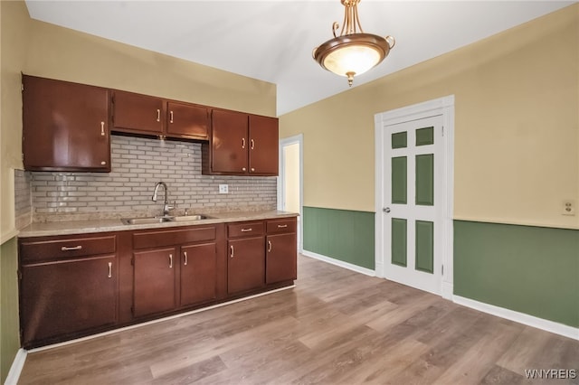 kitchen featuring dark brown cabinets, sink, decorative light fixtures, light wood-type flooring, and tasteful backsplash