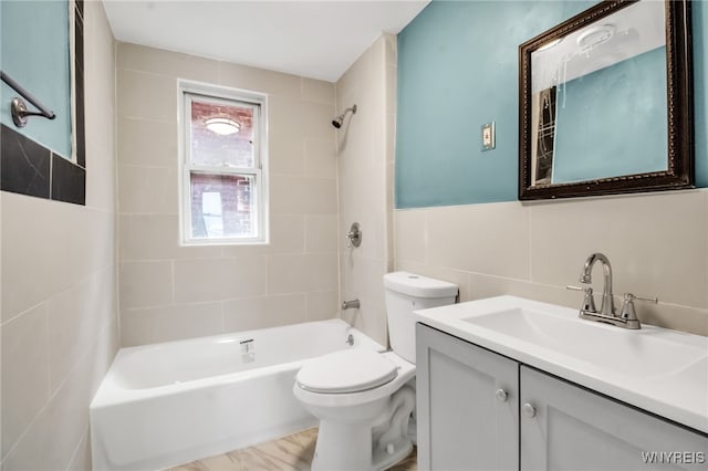 full bathroom with vanity, tiled shower / bath, toilet, and tile walls