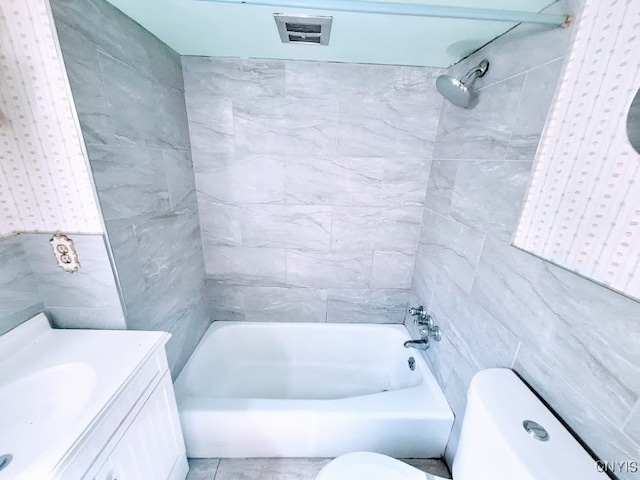 full bathroom featuring vanity, toilet, tiled shower / bath combo, and tile walls