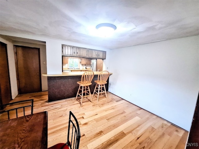 kitchen with light hardwood / wood-style floors, kitchen peninsula, stainless steel fridge, and a breakfast bar area