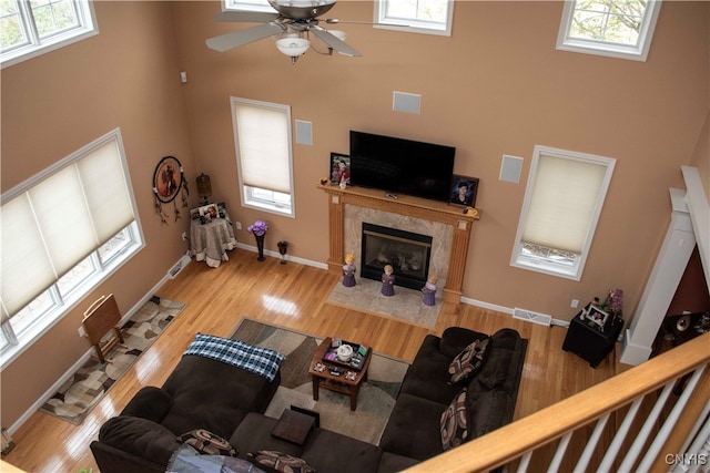 living room featuring ceiling fan, a towering ceiling, a high end fireplace, and light hardwood / wood-style flooring