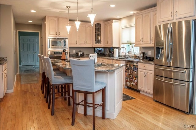 kitchen with a breakfast bar, an island with sink, sink, dark stone counters, and stainless steel appliances