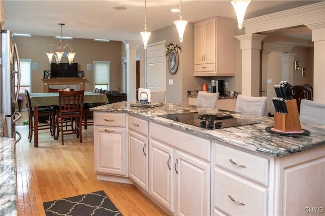 kitchen with decorative columns, stainless steel fridge, hanging light fixtures, light stone counters, and black electric cooktop