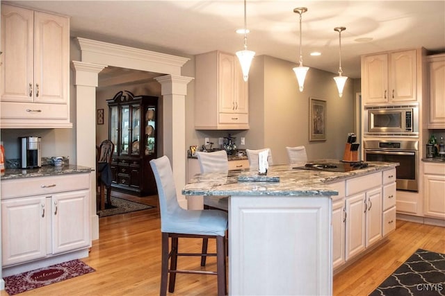 kitchen with stainless steel appliances, a center island, light stone counters, decorative light fixtures, and light wood-type flooring