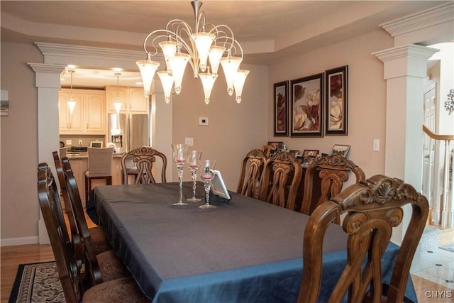 dining room with a tray ceiling, hardwood / wood-style flooring, a chandelier, and ornate columns