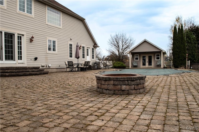 view of patio / terrace with a swimming pool with hot tub, an outbuilding, and a fire pit