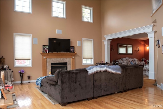 living room with ornate columns, a premium fireplace, a towering ceiling, and light wood-type flooring