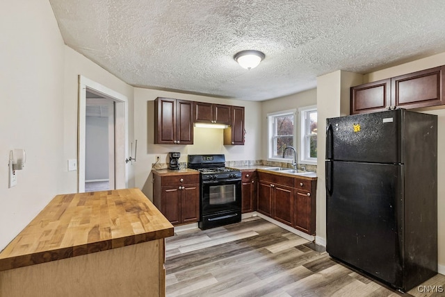 kitchen with a textured ceiling, black appliances, light hardwood / wood-style floors, sink, and butcher block countertops