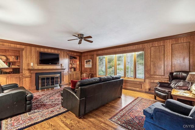 living room featuring ceiling fan, light wood-type flooring, wood walls, ornamental molding, and built in features