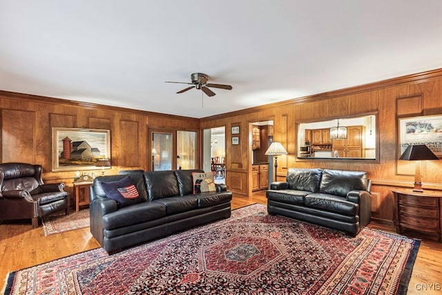 living room with ceiling fan, wood walls, ornamental molding, and light hardwood / wood-style flooring