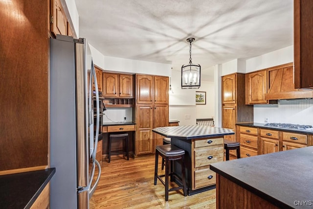 kitchen featuring gas stovetop, a kitchen island, light hardwood / wood-style flooring, decorative light fixtures, and stainless steel refrigerator