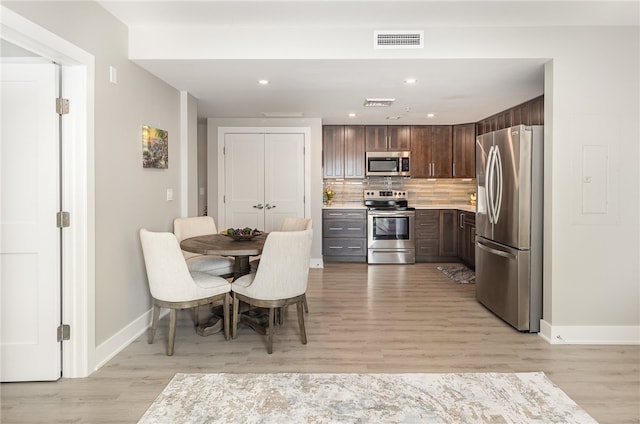 kitchen with backsplash, appliances with stainless steel finishes, dark brown cabinets, and light hardwood / wood-style floors