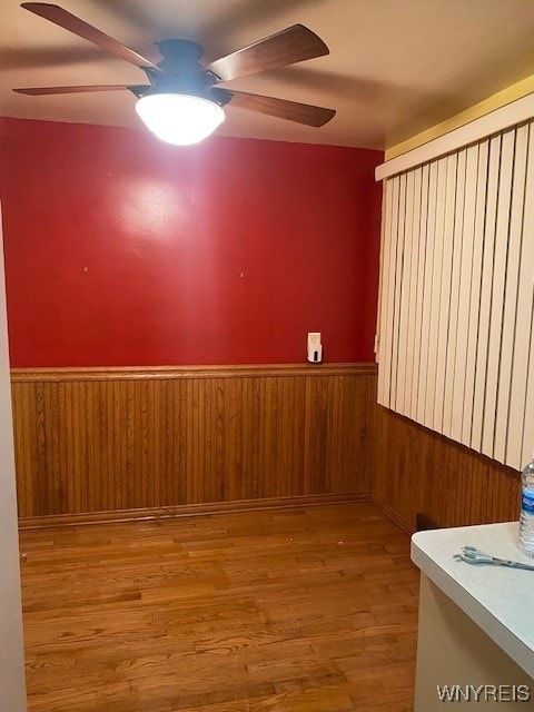 empty room with ceiling fan, wood-type flooring, and wooden walls