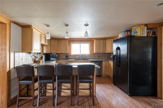 kitchen featuring stainless steel dishwasher, a breakfast bar, black refrigerator with ice dispenser, and hardwood / wood-style flooring