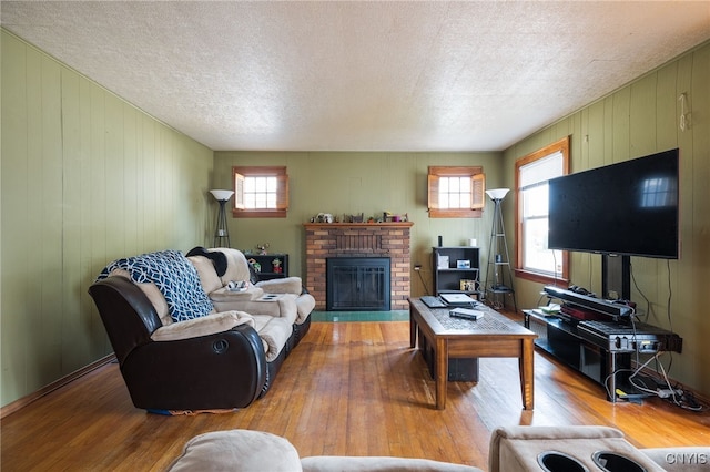 living room featuring a textured ceiling, hardwood / wood-style flooring, plenty of natural light, and a brick fireplace