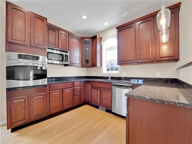 kitchen with appliances with stainless steel finishes, sink, hanging light fixtures, and light wood-type flooring