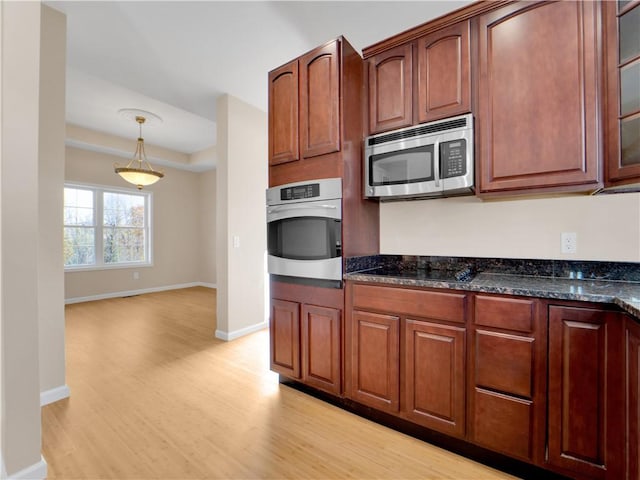 kitchen featuring decorative light fixtures, light hardwood / wood-style floors, dark stone counters, and appliances with stainless steel finishes