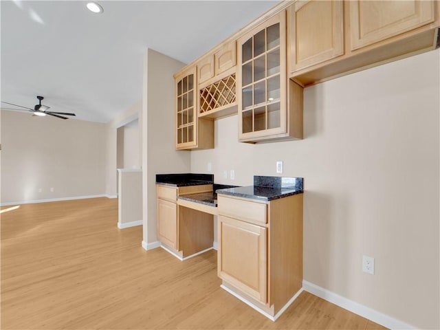 kitchen with dark stone countertops, light brown cabinetry, light hardwood / wood-style floors, and ceiling fan