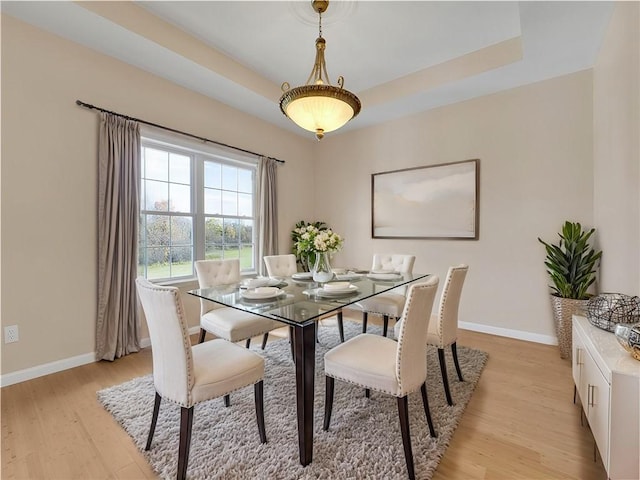 dining area with a raised ceiling and light hardwood / wood-style floors