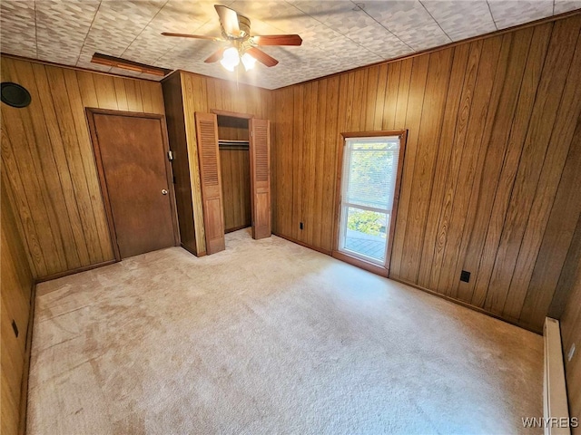 unfurnished bedroom featuring ceiling fan, light carpet, a baseboard heating unit, and wooden walls