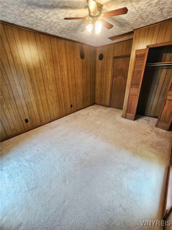 unfurnished bedroom featuring light carpet and wood walls