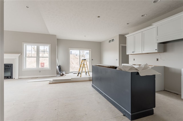 kitchen with a healthy amount of sunlight, a textured ceiling, a kitchen island, and white cabinets