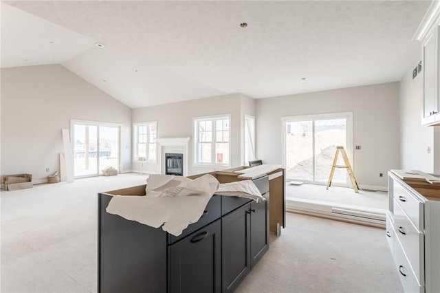 kitchen featuring a healthy amount of sunlight, vaulted ceiling, light colored carpet, and white cabinets