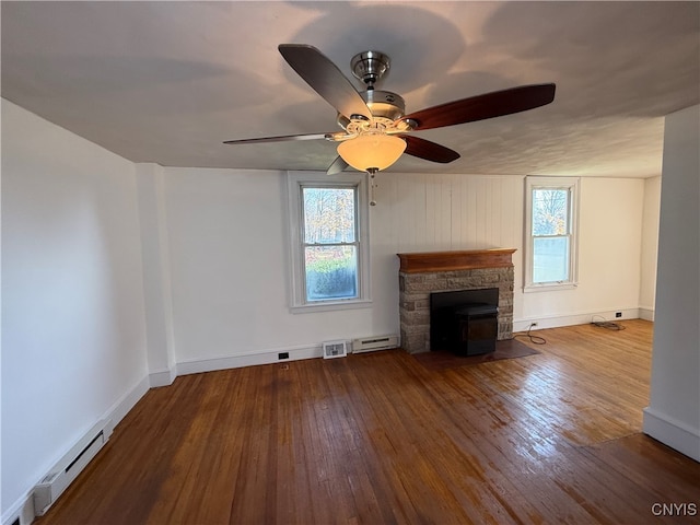 unfurnished living room with a wealth of natural light, baseboard heating, wood-type flooring, and ceiling fan