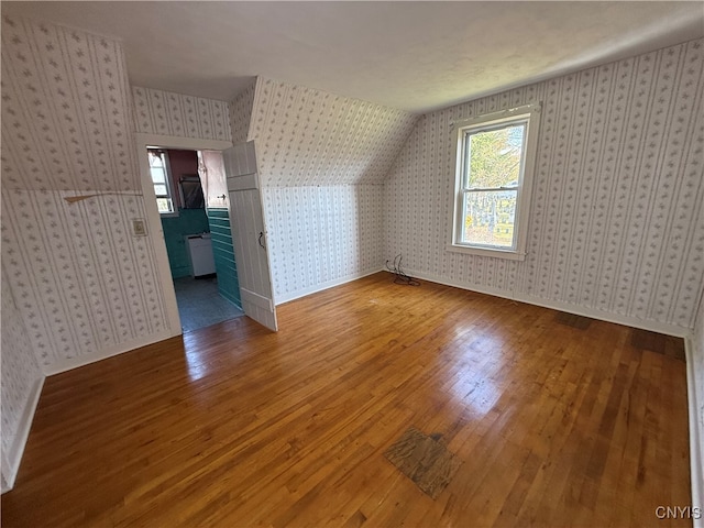 additional living space featuring a textured ceiling, lofted ceiling, and hardwood / wood-style floors