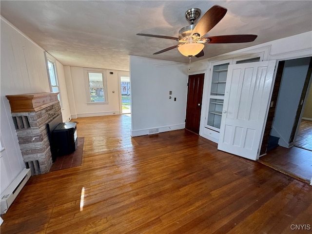 unfurnished living room featuring a baseboard heating unit, a stone fireplace, a textured ceiling, hardwood / wood-style floors, and ceiling fan